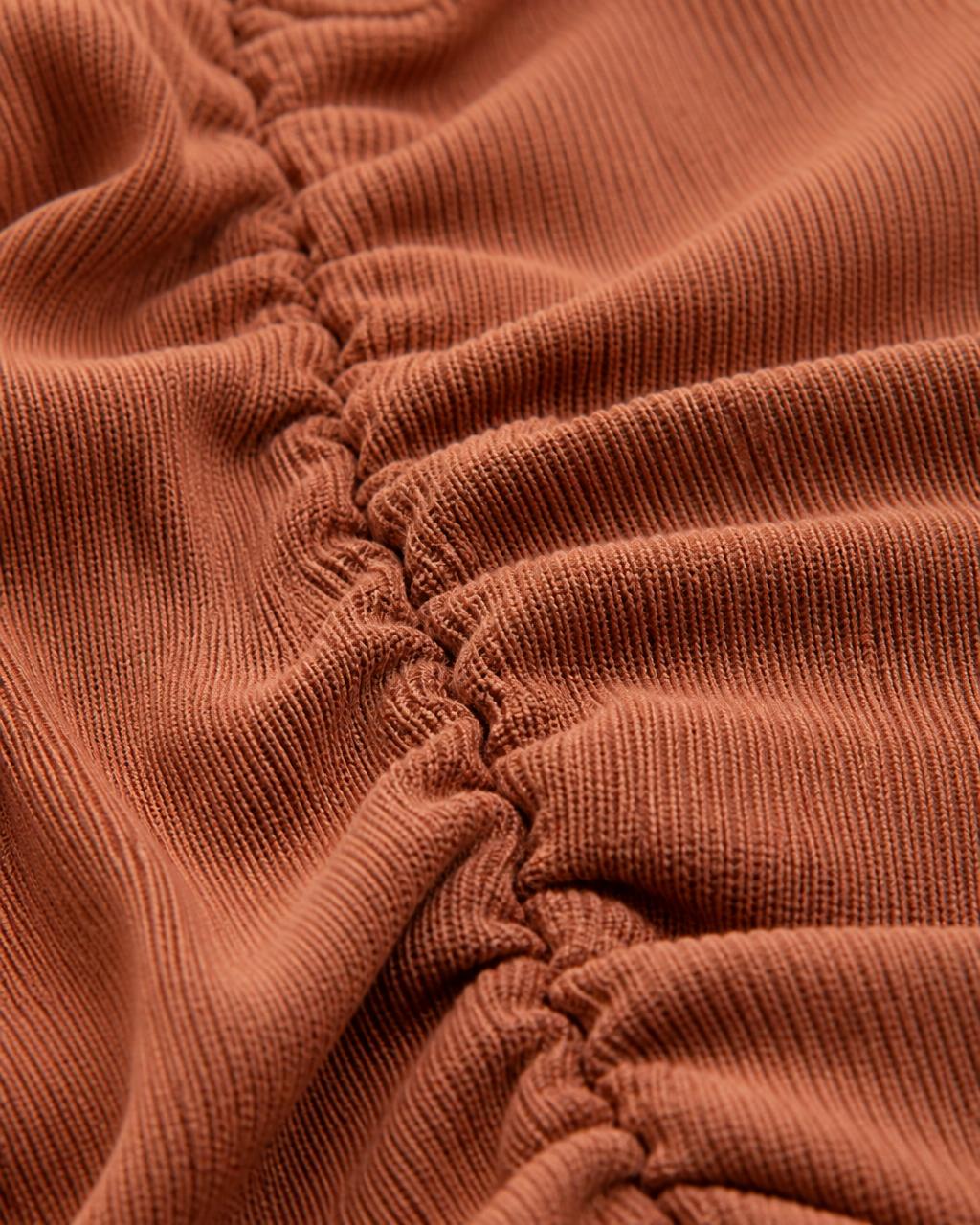 Macro detail of terracotta seamless ribbed knit and gathered scrunch seam