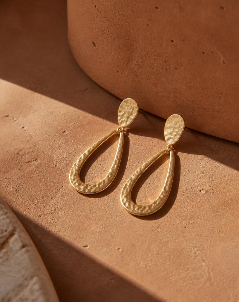 Minimalist gold drop earrings on terracotta surface