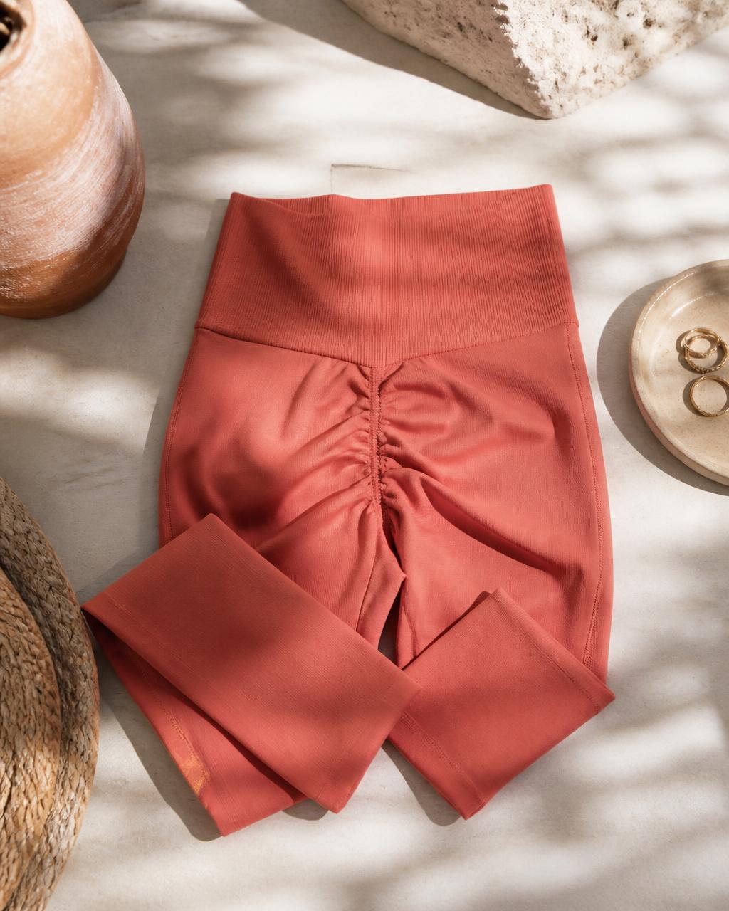 Coral seamless scrunch-back yoga tights, flat lay on sunlit stone